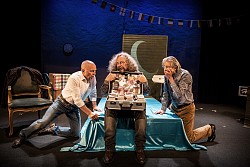 In der Mitte sitzt ein Mann mit geöffnetem Geldkoffer. Rechts und links davon knien zwei Männer mit erschrockenem Gesicht.