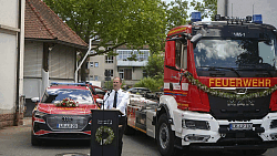 Der Feuerwehrkommandant bei seiner Rede. Er steht vor geschmückten Feuerwehrfahrzeugen.