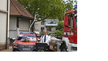 Der Feuerwehrkommandant bei seiner Rede. Er steht vor geschmückten Feuerwehrfahrzeugen.
