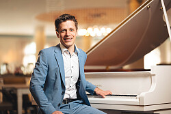 Benedikt Weigmann posiert vor einem weißen Piano.