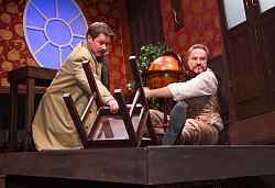 Zwei Männer kauern mit einem Stuhl und einem Globus in der Ecke eine Raumes.