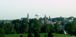 Das Bild zeigt einen Blick auf Belleville. Zu sehen sind über Bäumen links eine Kirche, in der Mitte ein weißer Wasserspeicher und rechts das Rathaus.