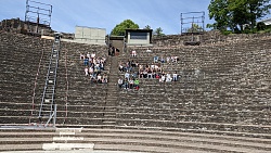 Schülerinnen und Schüler sitzen auf den Stufen eines Amphitheaters aus der Römerzeit. 
