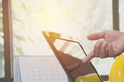 ein Laptop, daneben liegt ein gelber Bauhelm und eine Hand zeigt auf dem Bildschirm