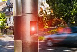Zu sehen ist ein Auto, das gerade an einem stationären Geschwindigkeitsmessegerät vorbeifährt und geblitzt wird.