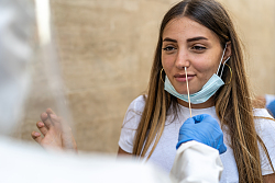 Eine junge lachende Frau bekommt gerade einen Nasenabstrich gemacht. 