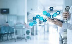 Tablet in der Hand vor einer Person in weißem Arztkittel.