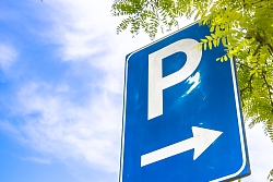 Ein blaues Parkplatzschild, umgeben von grün. 
