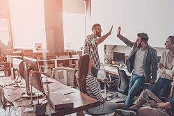 In einem Großraumbüro steht eine Gruppe von Menschen, die sich &#34;Give Fife&#34; geben. 