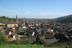 Das Bild zeigt einen Blick auf Lahr-Sulz. Links ist ein Kirchturm zu sehen, drumherum zahlreiche Häuser, dazwischen einige Bäume. Im Bildhintergrund sind bewaldete Berge zu erkennen. 