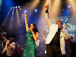 Eine Frau im grünen Kleid und ein Mann im Anzug singen auf einer Bühne